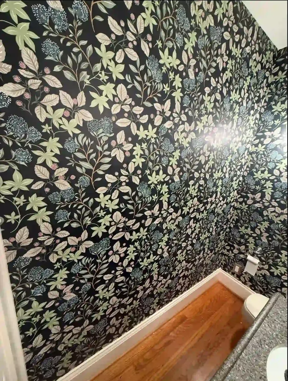 Dark leaf wallpaper on the walls of a powder room with a wood floor
